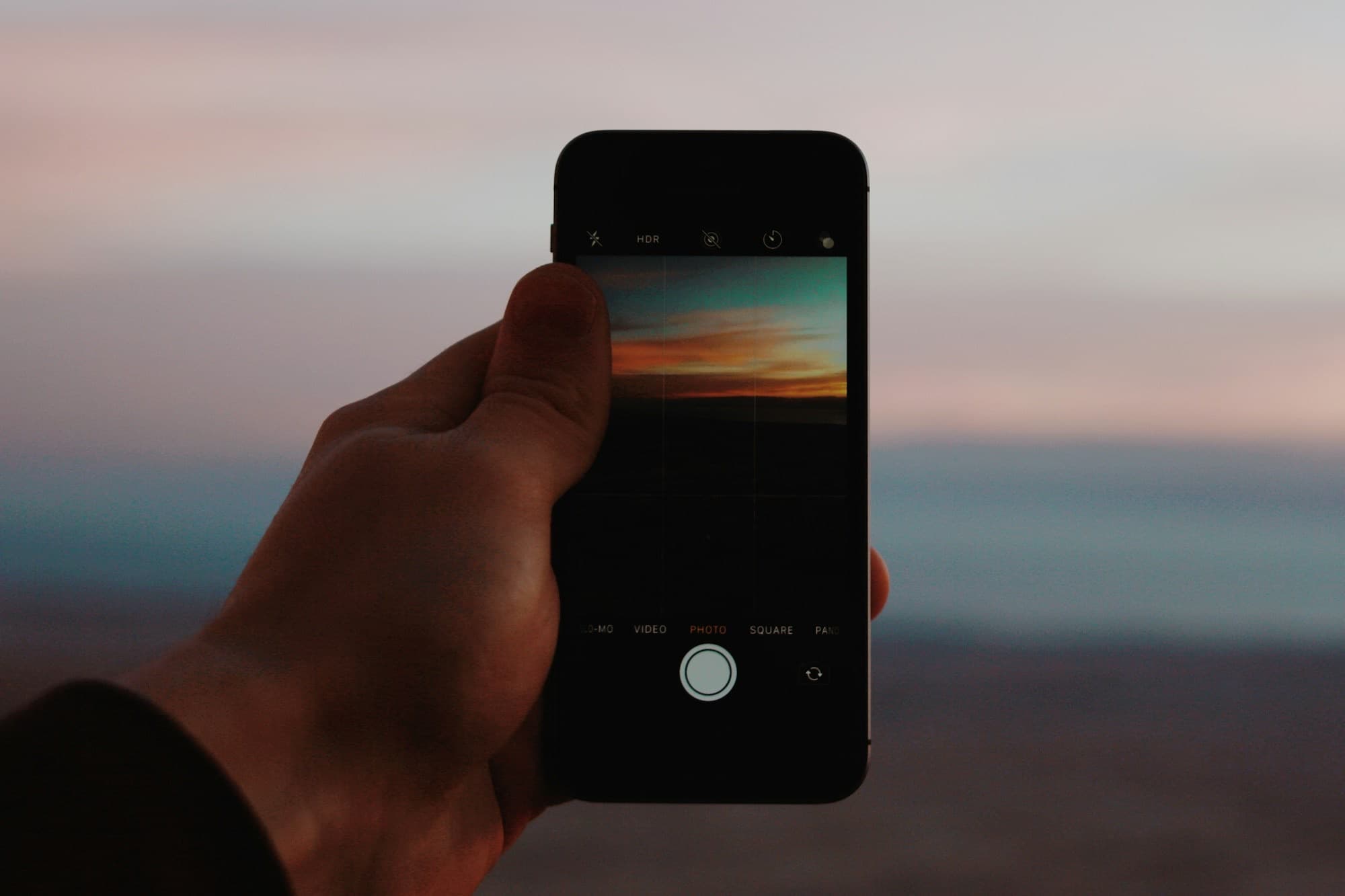 A hand holding a phone up against an evening sky
